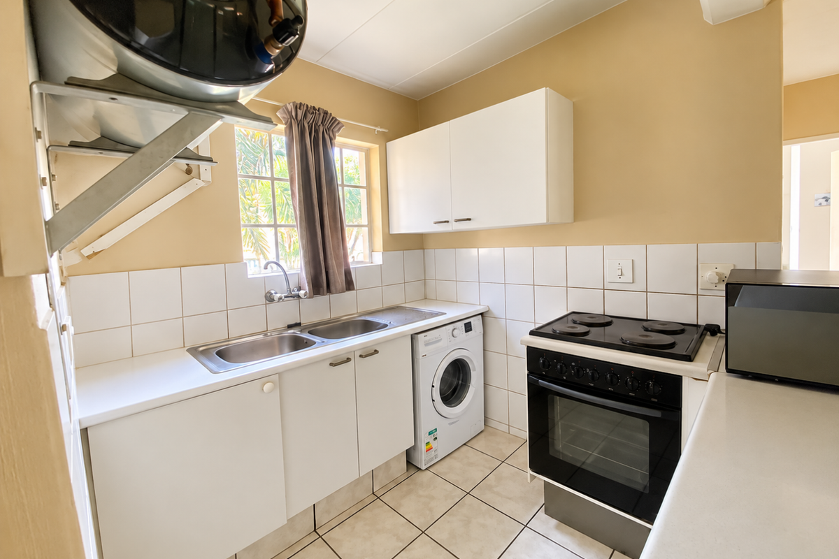 Functional kitchen featuring white cabinetry, tiled backsplash, stainless steel sink, and a built-in electric stove and oven.