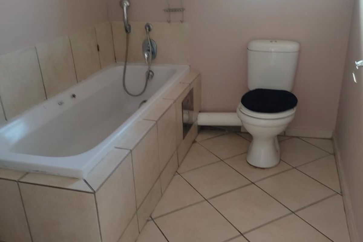 A functional bathroom featuring a built-in bathtub with tiled surround, a standard toilet, and tiled flooring.