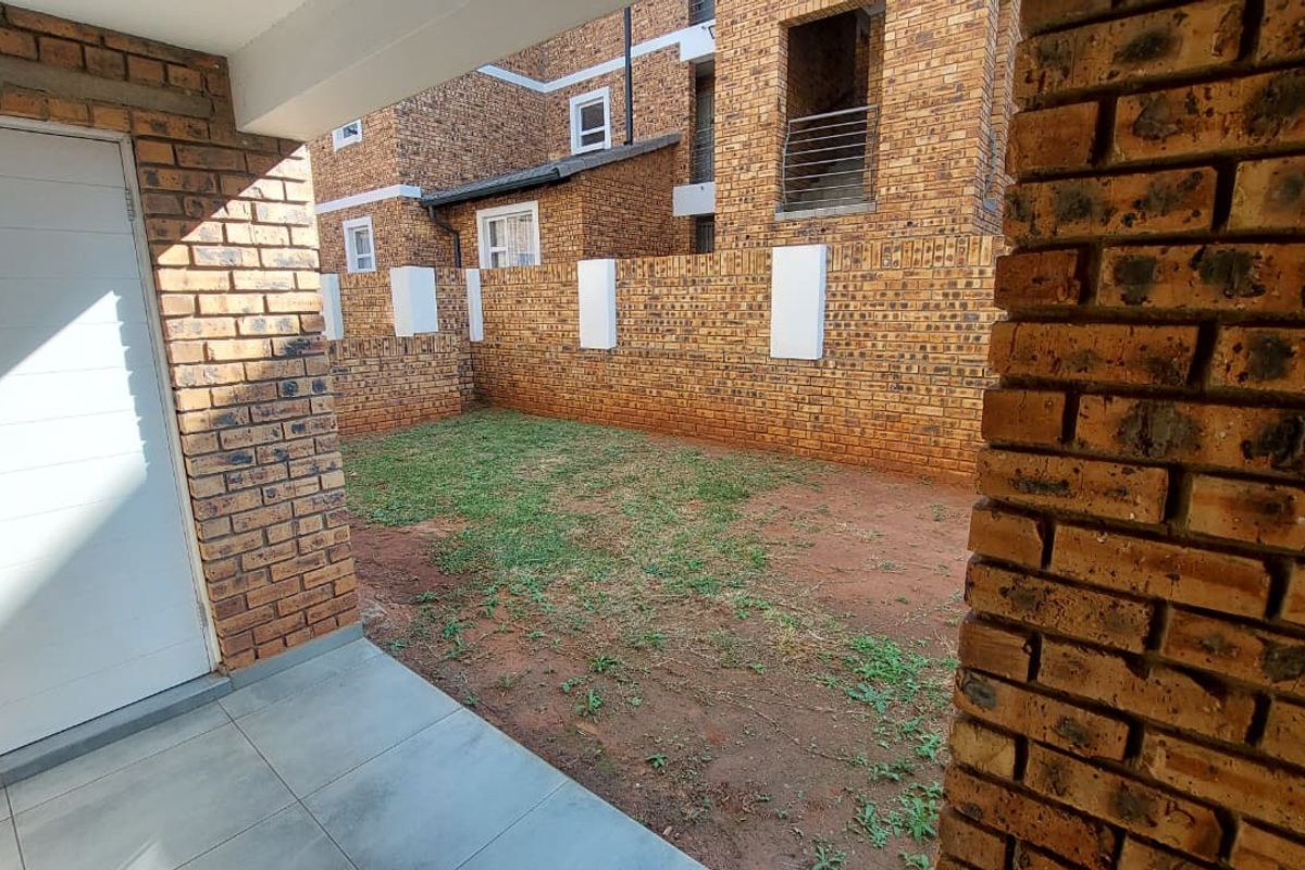 A private rear garden area featuring a tiled patio space and a brick boundary wall, viewed from the covered patio.