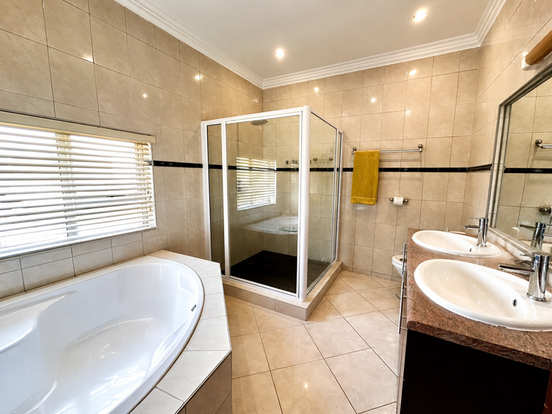 A well-maintained bathroom featuring a corner bathtub, a separate glass shower enclosure, and a double vanity with granite countertops.