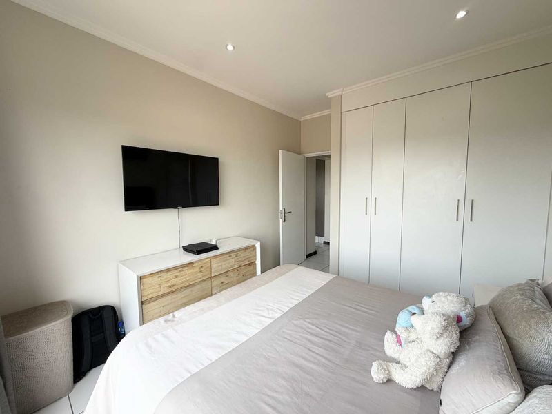 A well-maintained bedroom featuring neutral walls, tiled flooring, recessed downlighting, and ample built-in cupboard storage.