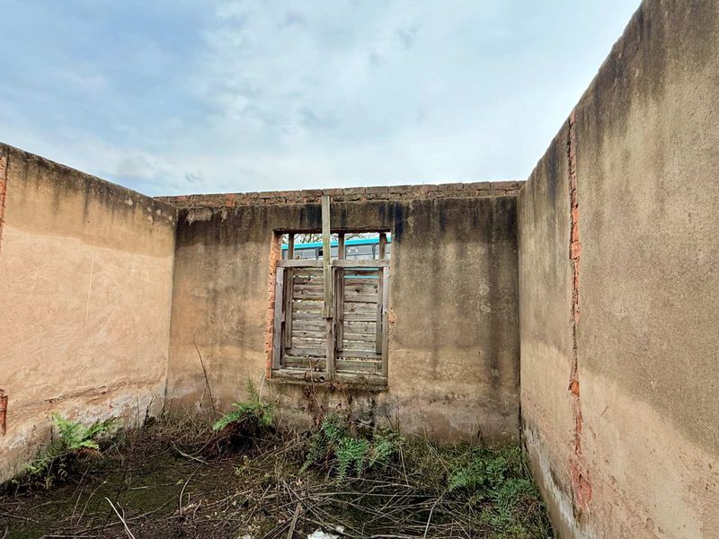 A derelict structure featuring exposed masonry walls and a weathered timber window frame, currently lacking a roof and in need of significant renovation.