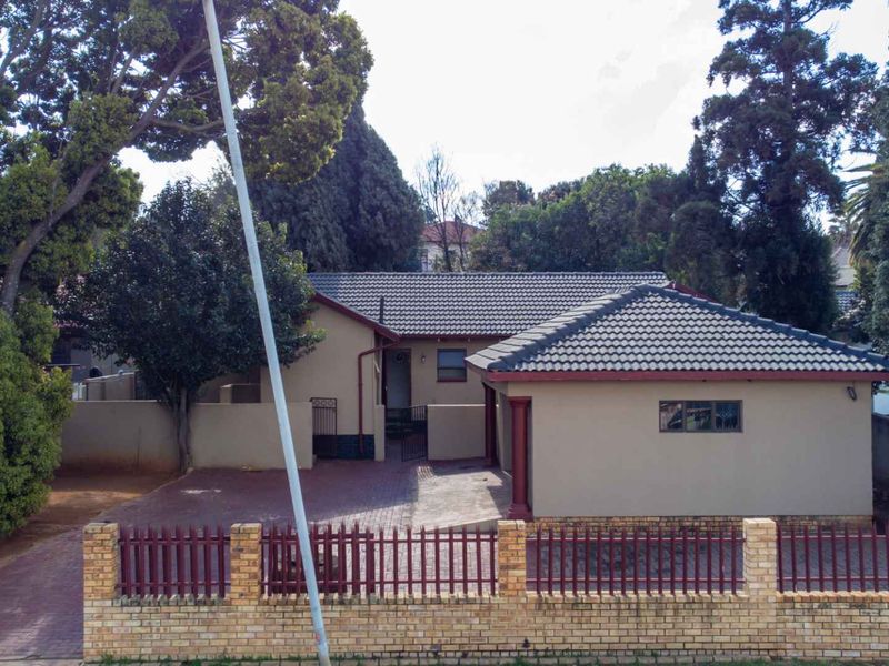 Front view of the property featuring a tiled roof, paved driveway, and a secure brick and metal boundary fence.