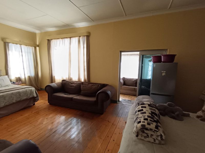 Spacious bedroom featuring original hardwood flooring, large windows with natural light, and direct access to an adjoining sunroom through a sliding glass door.