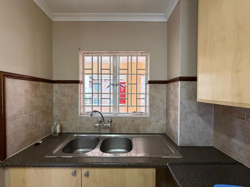 A functional kitchen area featuring a double bowl stainless steel sink, laminate cabinetry, and tiled splashbacks with security bars on the window.