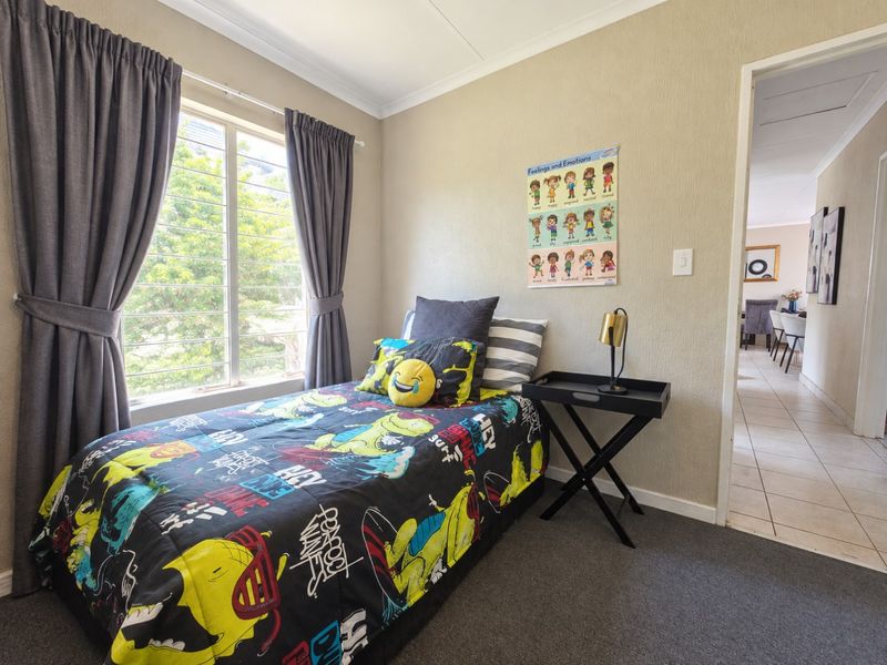 A functional bedroom featuring carpeted flooring, a large window with curtains, and coved ceiling detailing, providing a comfortable living space.