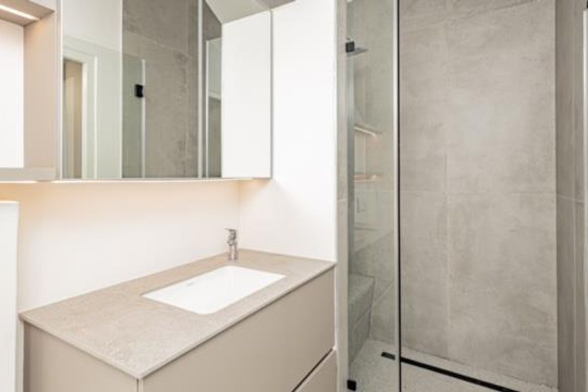 Modern bathroom featuring a sleek vanity with integrated sink, mirrored cabinetry, and a spacious walk-in shower with contemporary grey tiling.