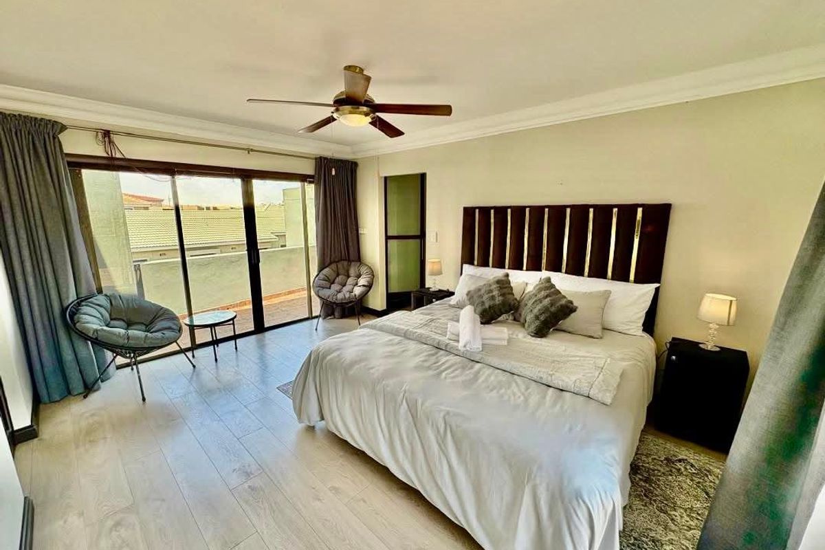 Spacious bedroom featuring light wood-look flooring, a ceiling fan, and large sliding glass doors providing access to a private balcony.