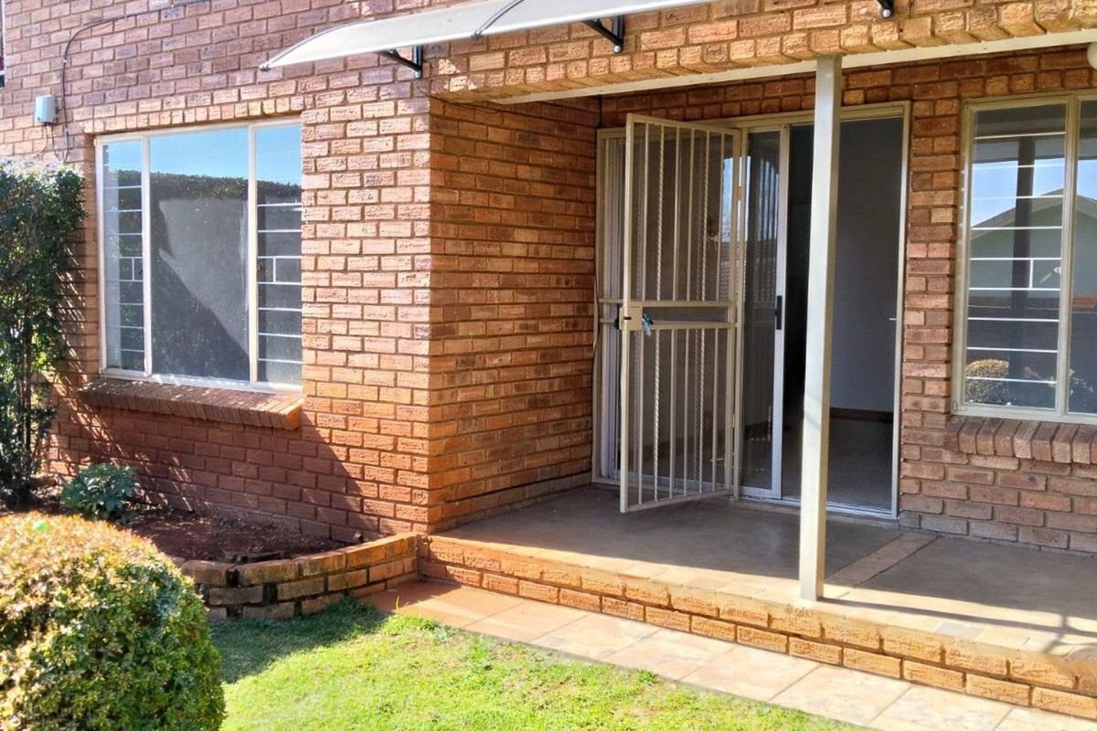 Rear exterior view of the townhouse featuring a face brick facade, a covered patio area, and secure sliding door access.