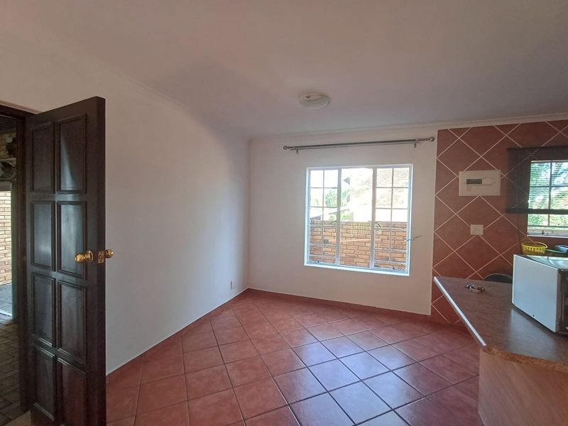 An open-plan living area featuring terracotta floor tiles, a tiled feature wall, and a breakfast bar, offering a functional and versatile space.