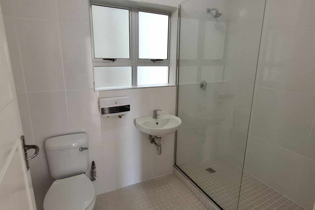A clean, functional bathroom featuring a glass-enclosed shower, wall-mounted basin, and toilet with neutral white wall tiling.