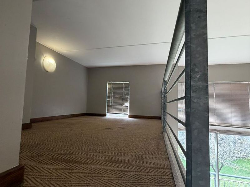 A mezzanine level bedroom area featuring carpeted flooring, a metal safety balustrade, and natural light through venetian blinds.