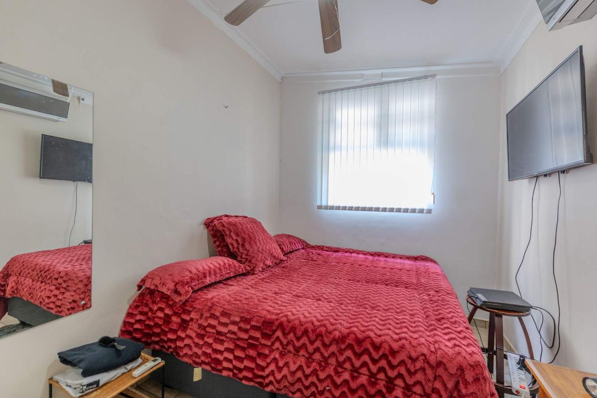 A compact bedroom featuring a ceiling fan, vertical blinds, and a wall-mounted air conditioning unit.