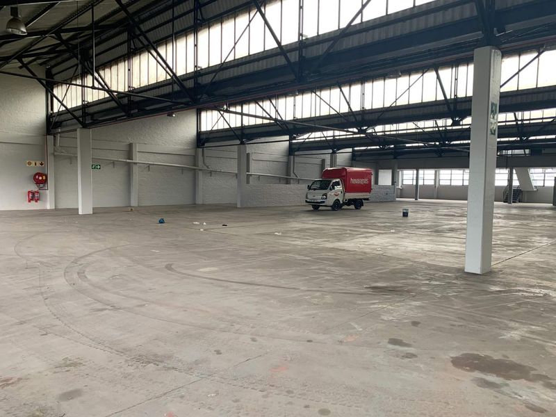 Spacious industrial warehouse featuring high ceilings with exposed steel trusses, clerestory windows for natural light, and durable concrete flooring.
