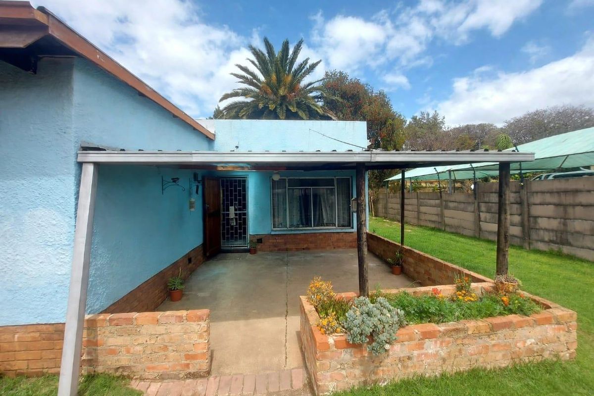 A rear exterior view featuring a covered patio area with brick planter boxes, concrete flooring, and a secure entrance door.