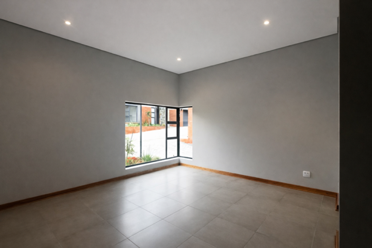 A bright, empty room featuring neutral grey walls, tiled flooring, and a corner window providing natural light and a view of the exterior.
