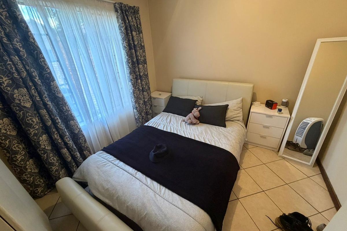 A cozy bedroom featuring tiled flooring and a large window with curtains, providing natural light and a comfortable living space.