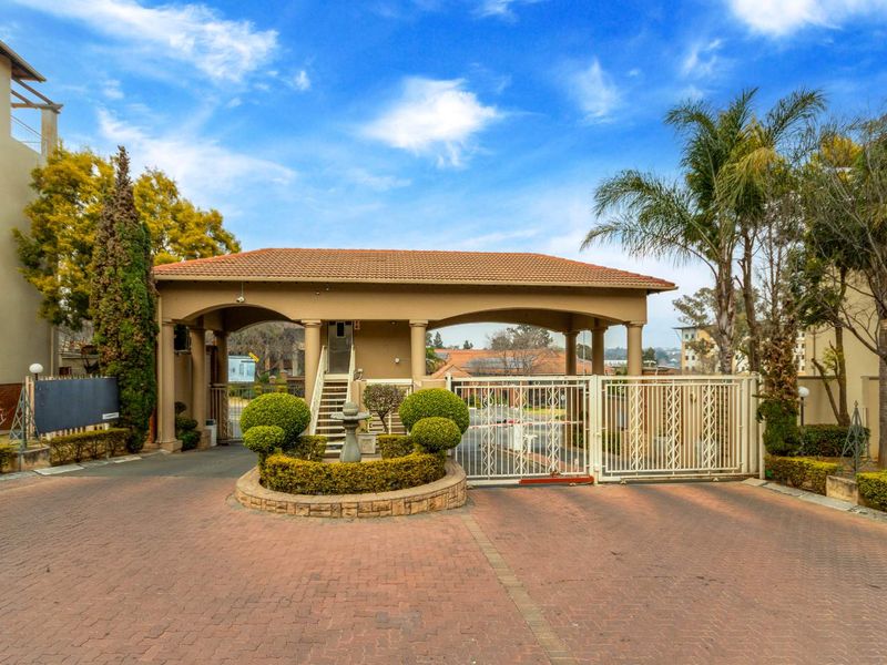 The apartment complex features a secure gated entrance with a paved driveway, covered portico, and well-maintained landscaped garden area.