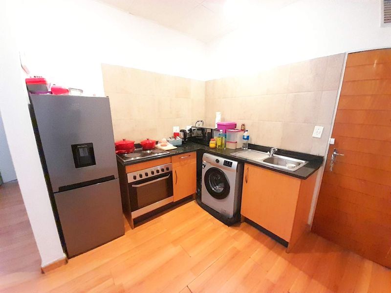 Compact kitchen featuring wooden cabinetry, laminate countertops, tiled backsplash, and integrated cooking appliances, providing a functional workspace.