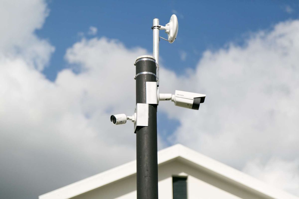 A close-up view of a security pole equipped with multiple surveillance cameras and a wireless antenna, positioned against a clear sky.