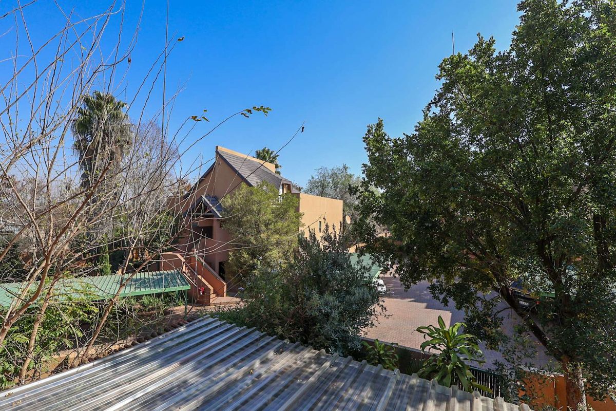 An elevated view of the property exterior, featuring a paved driveway, carport structure, and surrounding mature trees.