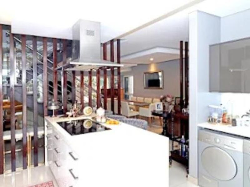 Modern open-plan kitchen and living area featuring a central island, sleek cabinetry, and a decorative timber slat divider separating the staircase.