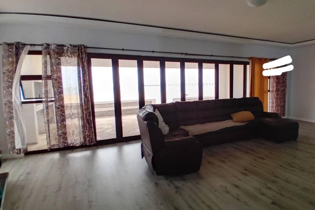 Spacious living room featuring modern laminate flooring and expansive folding glass doors that provide ample natural light and access to the outdoors.