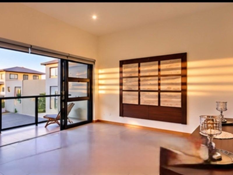 Spacious living area featuring large sliding glass doors opening onto a balcony, complemented by modern tiled flooring and integrated wall cabinetry.