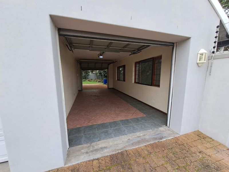 A spacious, drive-through garage featuring tiled flooring, a sectional door, and direct access to the rear garden area.