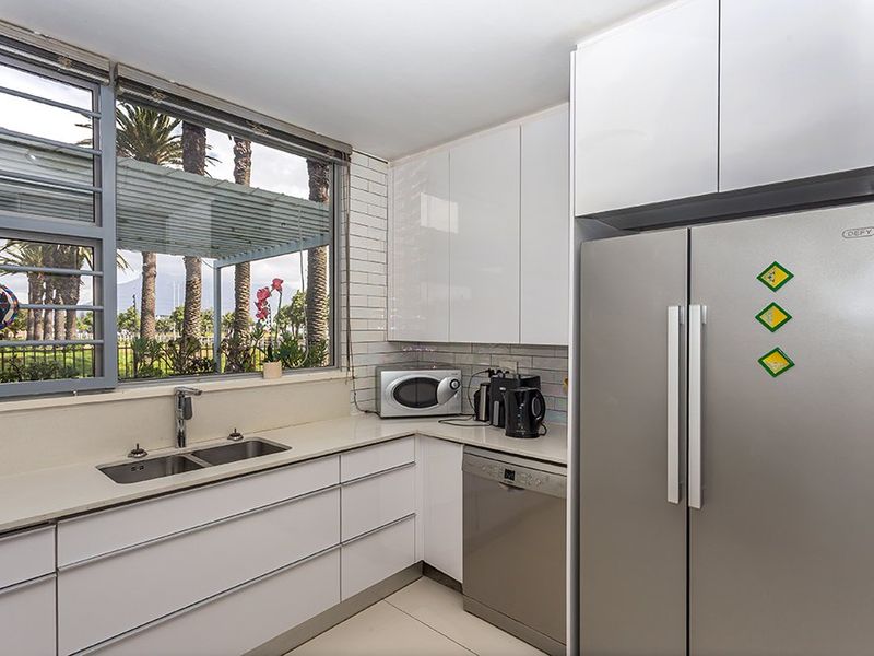 Modern kitchen featuring sleek white cabinetry, stone countertops, subway tile backsplash, and integrated appliances with a large window overlooking the garden.