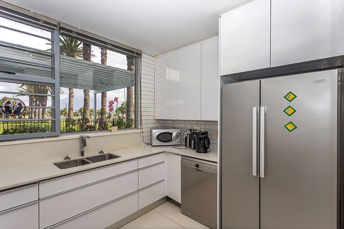 Modern kitchen featuring sleek white cabinetry, stone countertops, subway tile backsplash, and integrated appliances with a large window overlooking the garden.