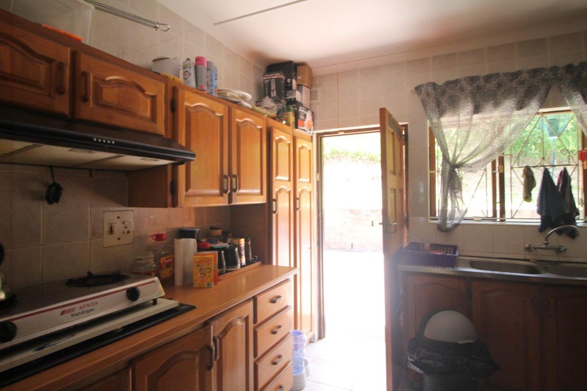 A functional kitchen featuring wooden cabinetry, tiled walls, and direct access to the exterior, offering a practical layout for daily meal preparation.