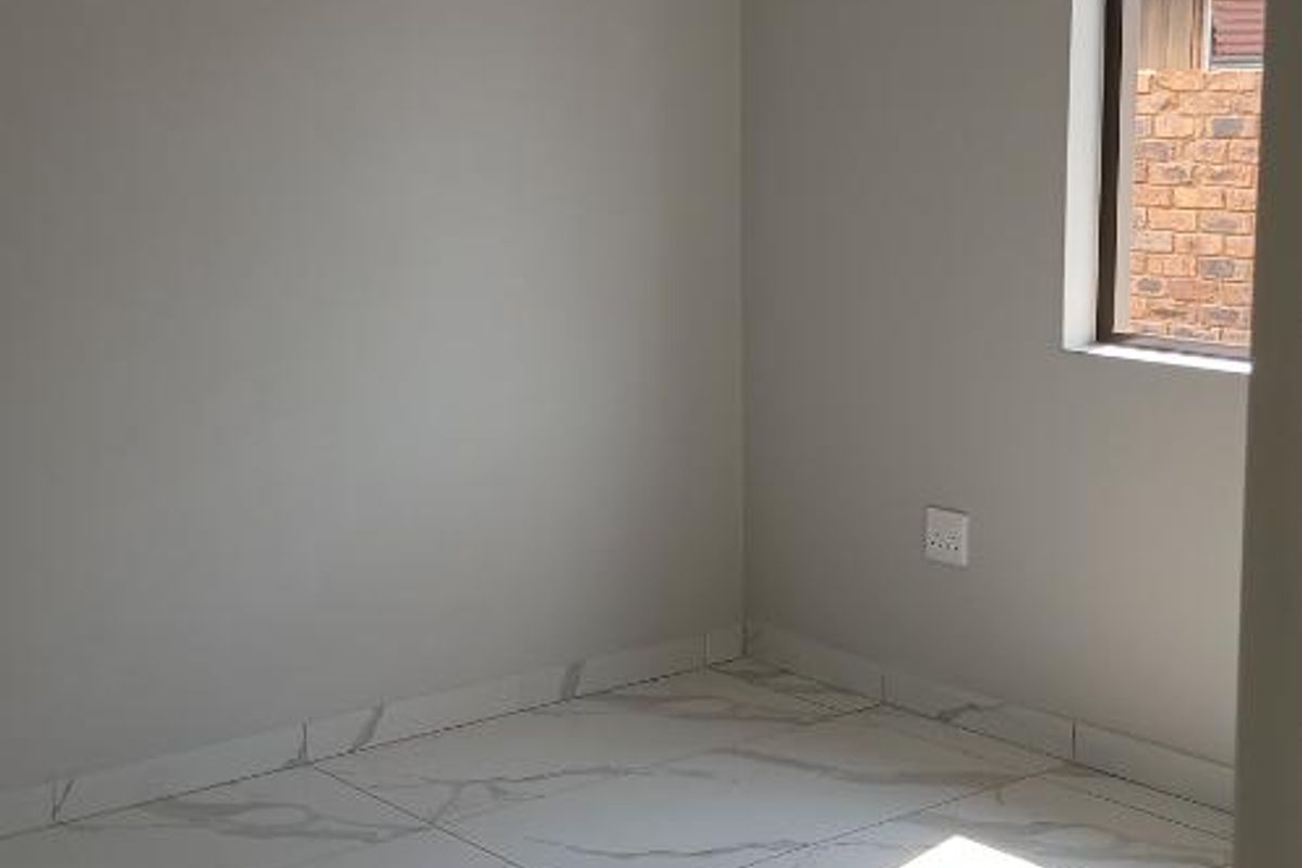 A bright, empty bedroom featuring modern marble-look porcelain floor tiles, neutral wall finishes, and a flush mount ceiling light.