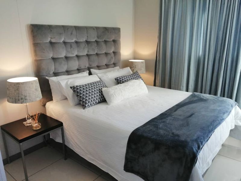 A well-maintained bedroom featuring neutral tiled flooring and floor-to-ceiling curtains, providing a clean and comfortable living space.