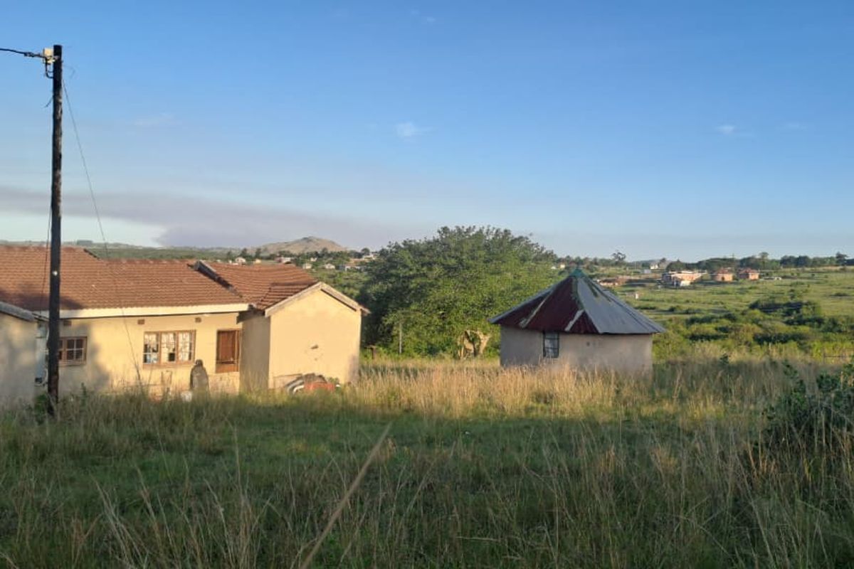 A rural property featuring a main house and a separate rondavel structure set within a large, open grassy landscape.
