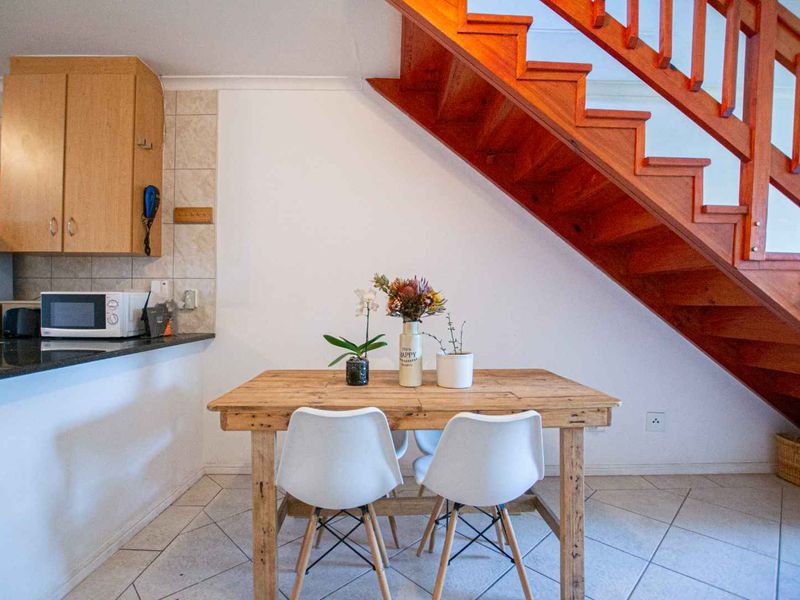 Open plan kitchen and dining area featuring tiled flooring, granite countertops, and a prominent wooden staircase leading to the upper level.