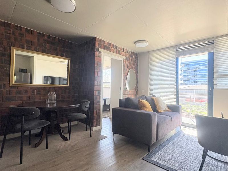 A well-lit living area featuring an exposed brick wall, laminate flooring, and a sliding glass door leading to an outdoor space.