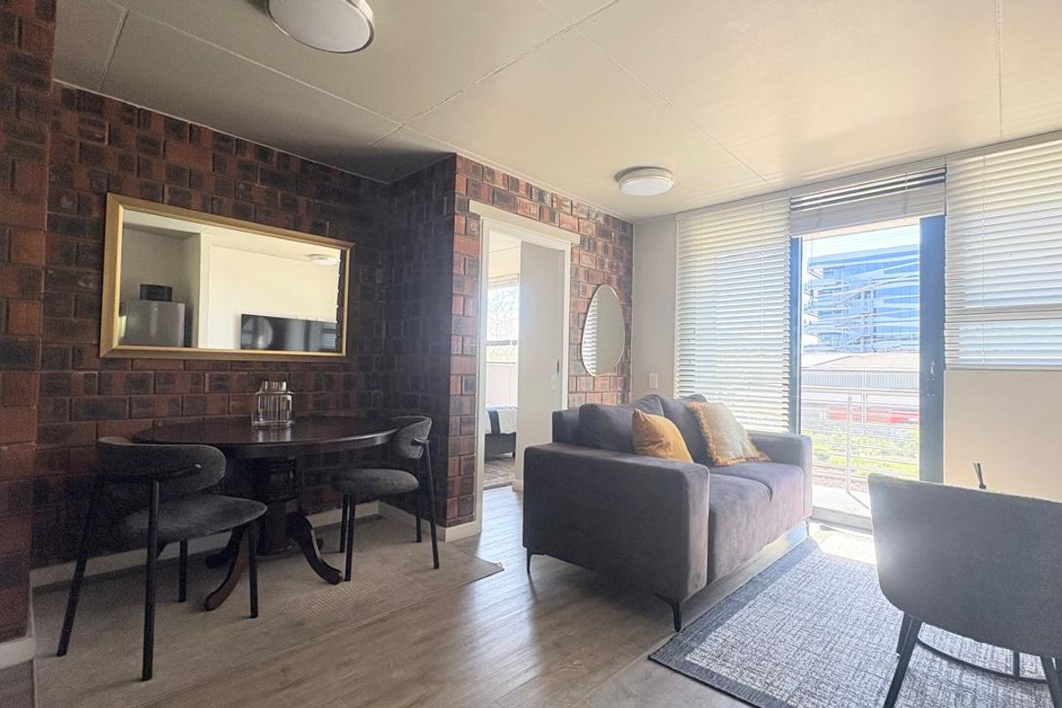 A well-lit living area featuring an exposed brick wall, laminate flooring, and a sliding glass door leading to an outdoor space.