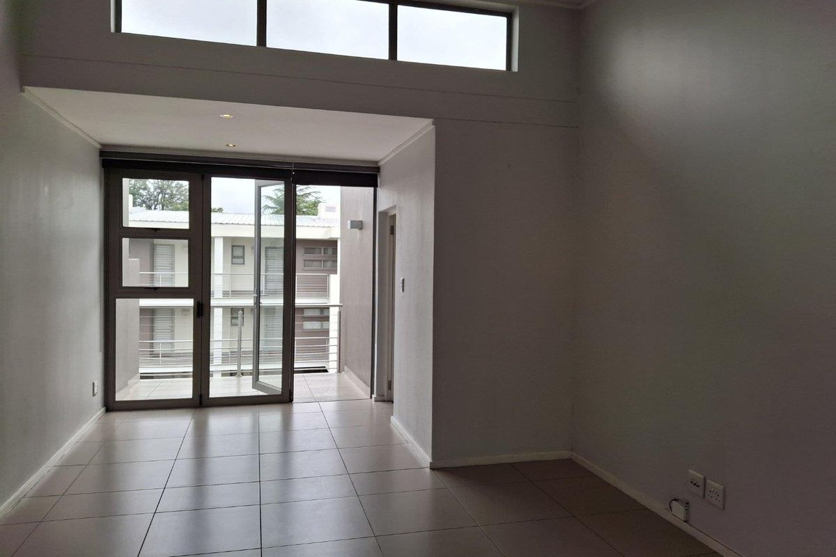 A bright, empty living area featuring large aluminium-framed glass doors leading to a balcony, tiled floors, and high-level clerestory windows for natural light.