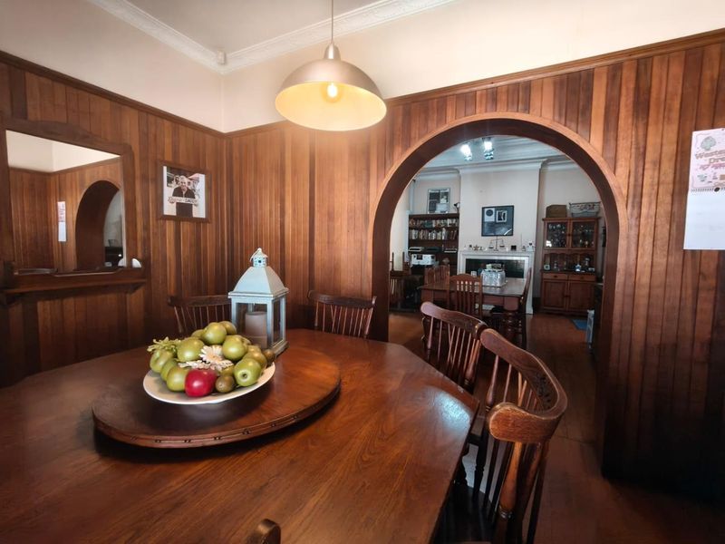 Dining room featuring extensive timber wall paneling, a classic archway leading to an adjoining living space, and a traditional fireplace.