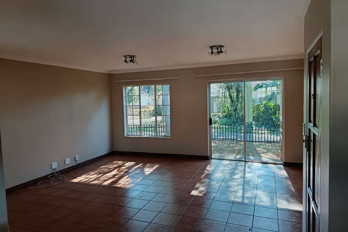 Spacious, empty living room featuring tiled flooring, large windows, and a sliding glass door providing access to the garden area.