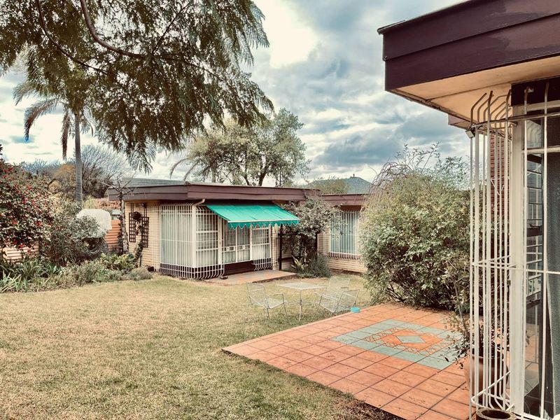 A rear garden view featuring a tiled patio area, security bars on windows, and a retractable awning over a secondary building entrance.