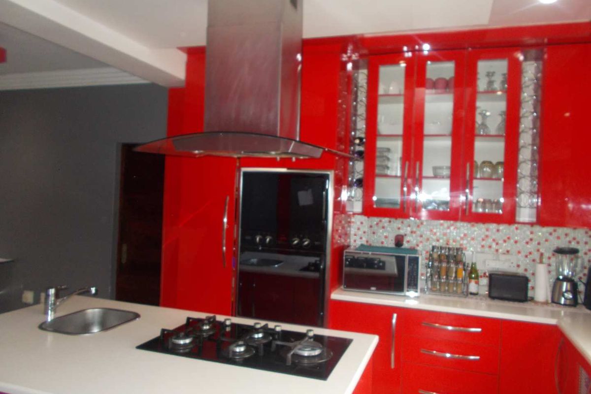 Modern kitchen featuring vibrant red cabinetry, a central island with a built-in gas hob and sink, and a stainless steel extractor fan.