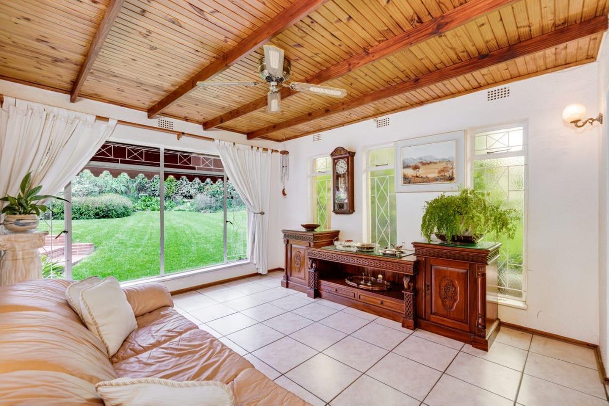 A bright living room featuring a vaulted timber-paneled ceiling, tiled flooring, and large windows providing views of the garden.