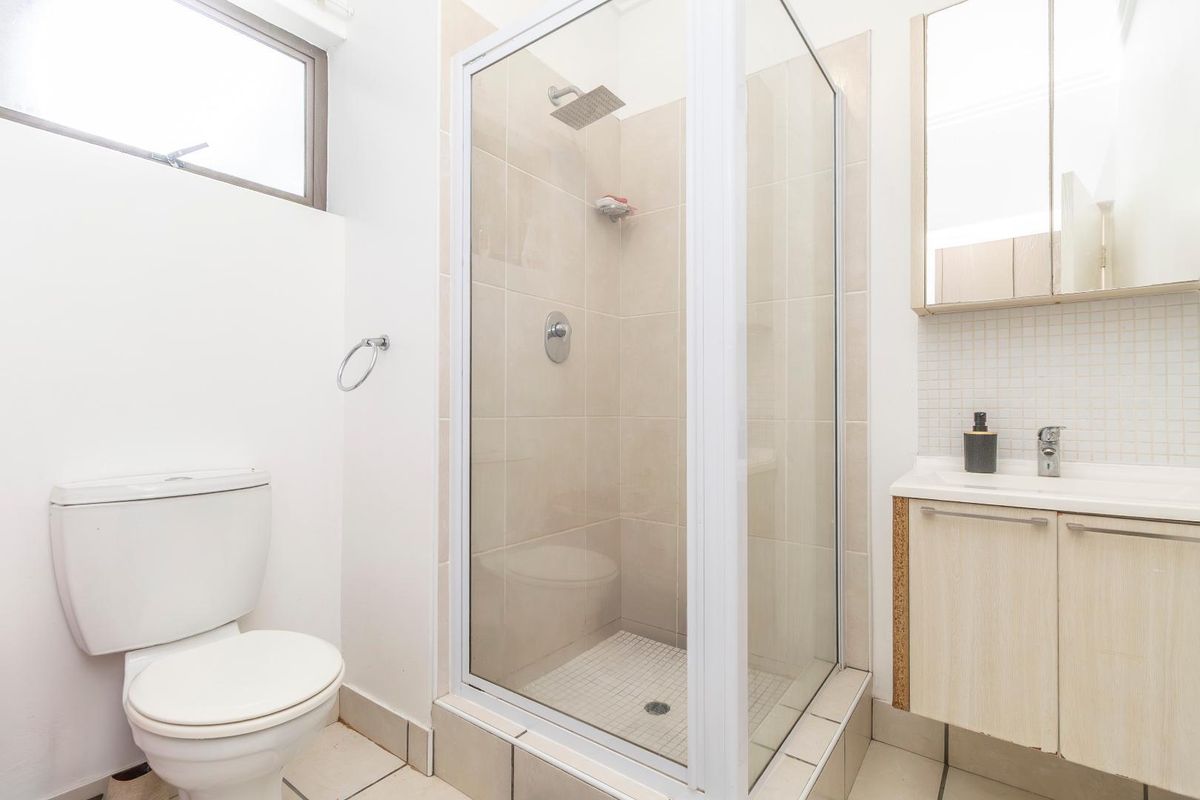 A functional bathroom featuring a glass-enclosed shower, a white toilet, and a vanity cabinet with a basin and mirror.