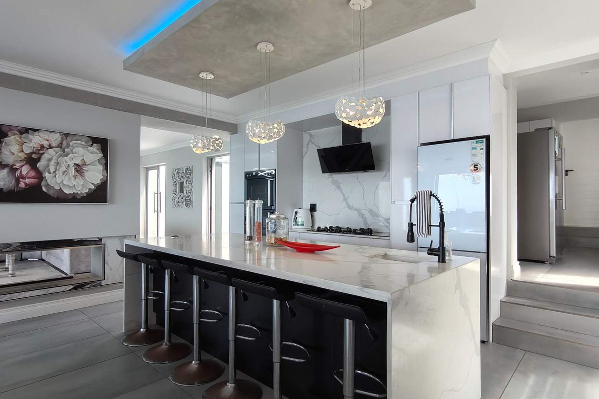 Modern, high-end kitchen featuring a large marble waterfall island, sleek cabinetry, integrated appliances, and a stylish recessed ceiling with ambient LED lighting.