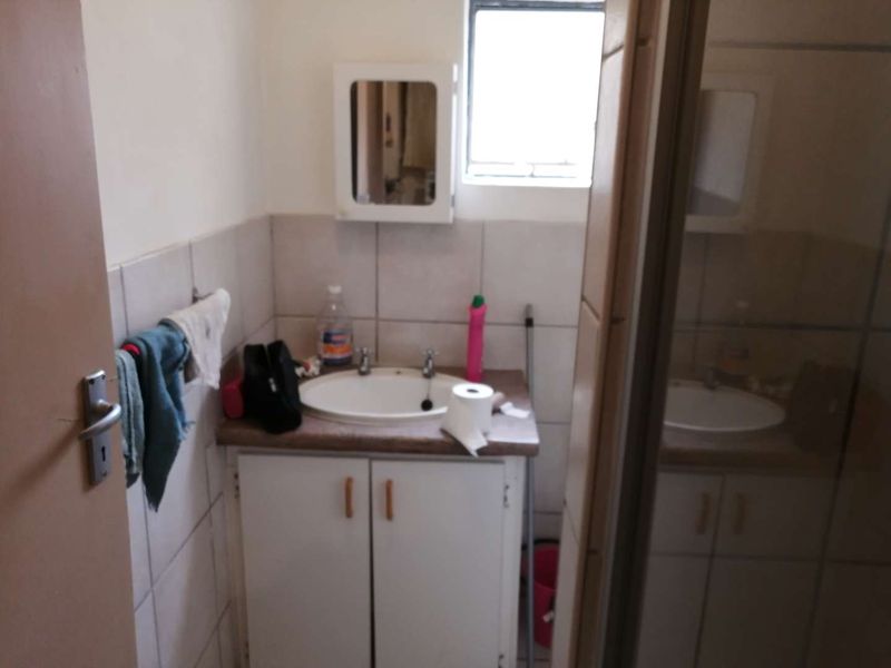 A compact bathroom featuring a vanity cabinet with a basin, tiled walls, and a wall-mounted medicine cabinet.