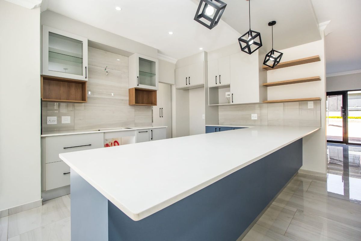 Modern kitchen featuring a large island with quartz countertops, sleek cabinetry, floating shelves, and contemporary pendant lighting in a bright, open-plan space.