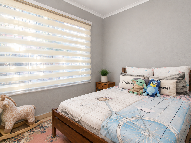 A well-maintained bedroom featuring neutral grey walls, a large window with modern zebra blinds, and classic cove cornice detailing.