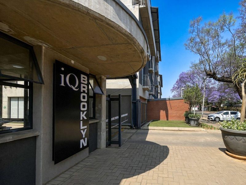 Entrance area of iQ Brooklyn apartment complex featuring a concrete overhang, paved driveway, and secure access gate.